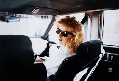 一位身穿白衬衫、戴着黑色太阳镜的女士坐在汽车座椅上